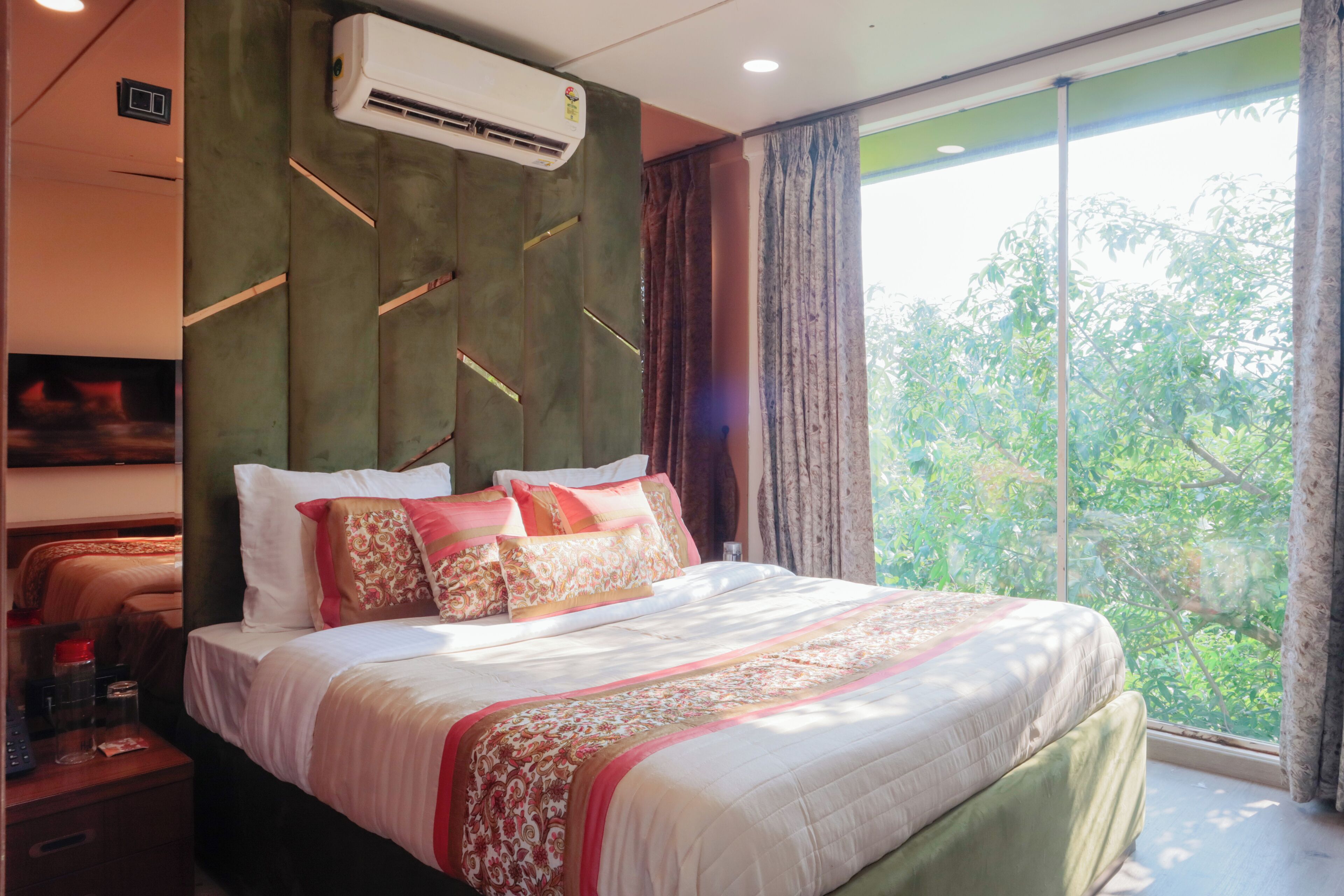 Habitación de hotel con una cama grande, aire acondicionado de pared y ventana con vista a árboles.