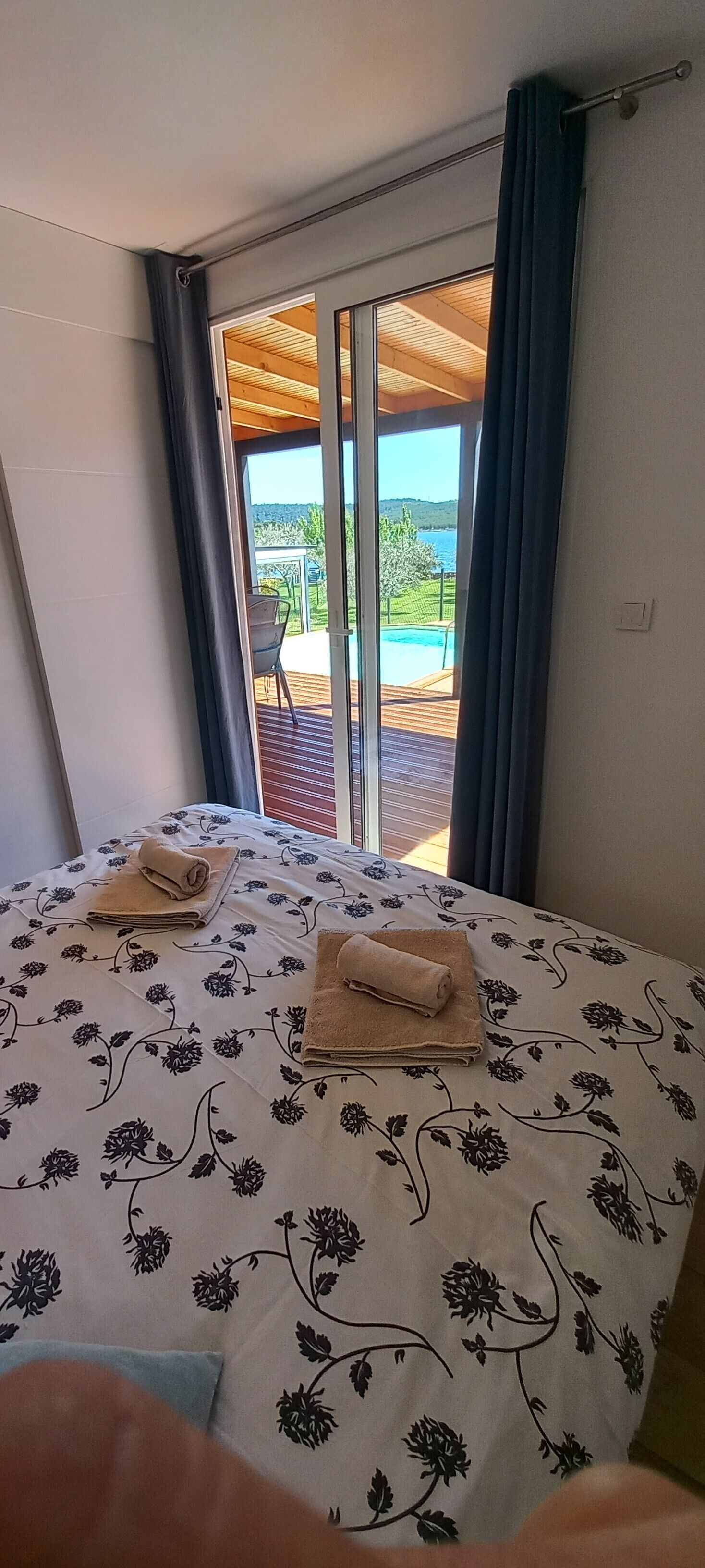 Camera da letto con un letto grande, due asciugamani e vista su una piscina e vegetazione attraverso una porta scorrevole in vetro.