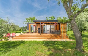A modern house with a wooden deck, outdoor seating, and a large tree. - Beach houses Ive & Beta – romantic oasis, pool, jacuzzi, privacy, near to sea (Pula)