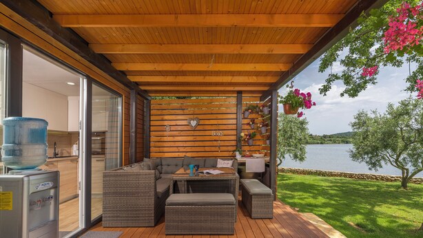 Un espacio de estar al aire libre cubierto con techo de madera, muebles de mimbre y vista a un lago.