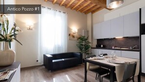 A modern kitchen with white cabinets and a dark countertop. There is a dining table set for two with plates and glasses. - Ancient Well 1 | Villa Carobbi Apt (Firenze)
