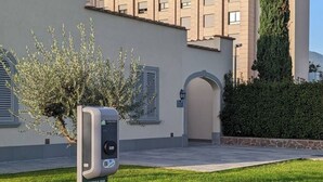 A building with a modern facade, a paved entrance, and a charging station in the foreground. - Ancient Well 1 | Villa Carobbi Apt (Firenze)