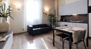 A modern kitchen with white cabinets and a dark countertop. There is a dining table set for two with plates and glasses.