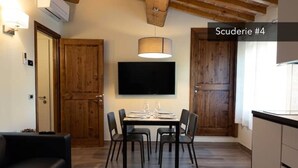 A dining area with a table set for four, a flat-screen TV mounted above, and wooden doors. - Stables 4 | Apartment Villa Carobbi (Firenze)