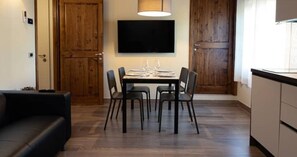 A dining area with a table set for four, a flat-screen TV mounted above, and wooden doors. - Stables 4 | Apartment Villa Carobbi (Firenze)