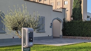 A charging station in front of a building with a paved walkway, a tree, and a hedge. - Ancient Well 3 | Villa Carobbi Apt (Firenze)