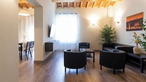 A modern living room with wooden flooring, a flat-screen TV mounted on the wall, and a dining area with chairs and a table. - Ancient Well 3 | Villa Carobbi Apt (Firenze)