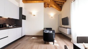 Une cuisine moderne avec des armoires blanches, un plan de travail noir et un plafond en bois. On trouve une chaise noire au centre de la pièce et un téléviseur à écran plat fixé au mur.