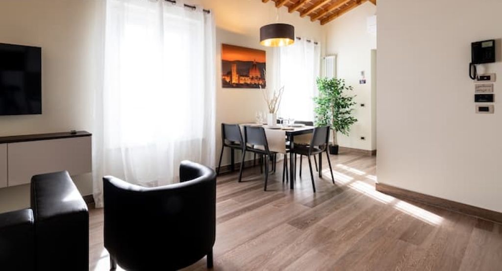Een moderne woonkamer met een houten plafond, een eethoek met een tafel en stoelen, en een aan de muur bevestigde televisie.