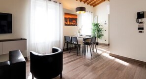A modern living room with a wooden ceiling, a dining area with a table and chairs, and a TV mounted on the wall. - Ancient Well 2 | Villa Carobbi Apt (Firenze)