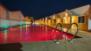 Ein Swimmingpool mit einem rot beleuchteten Wasserspiel, umgeben von Hotelzimmern mit einheitlichem Baustil.