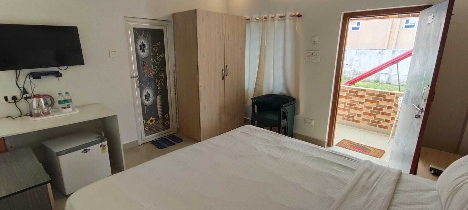 A bedroom with a bed, a TV, a desk with a kettle, a small fridge, and a door with floral artwork.