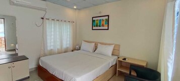 A hotel room with a bed, a desk, a chair, a wardrobe, and a window with curtains.