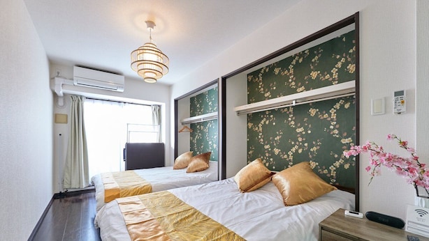 A hotel room with two beds, a bedside table, a lamp, an air conditioning unit, and a window with curtains. - XS16 XROSS STAY Namba8 (大阪市中央区島之内)