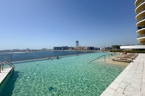 Una piscina cristalina con vistas al mar y al horizonte de la ciudad.