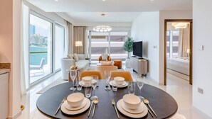 A modern living room with a dining area set for four, large windows, and a view of the city.