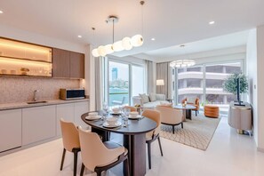 A modern hotel room with a dining area, a sofa set, and a view of the city.