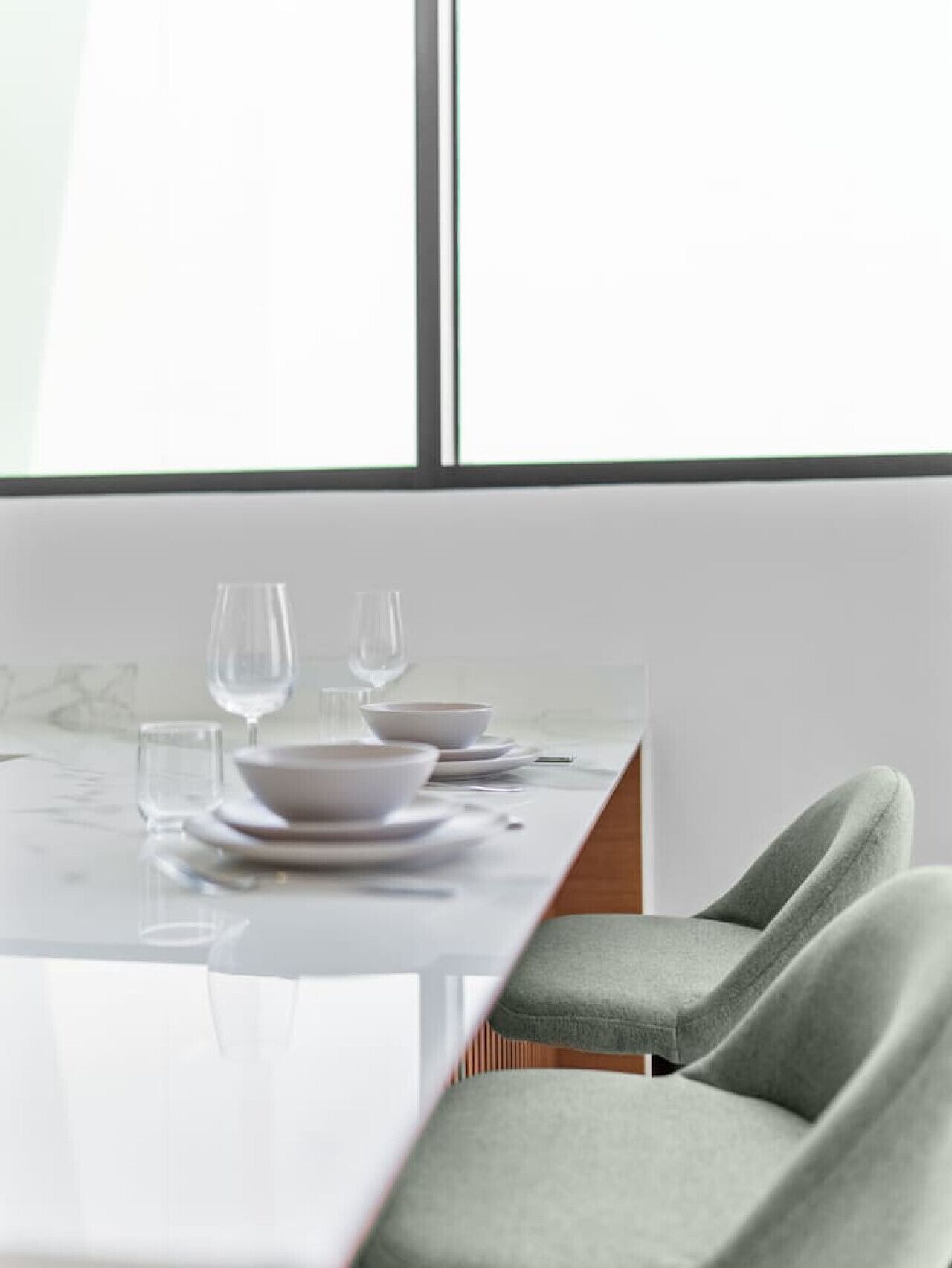 Una mesa de comedor dispuesta con platos, tazones y vasos, con una ventana al fondo.