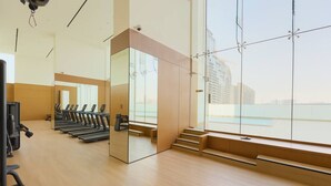 A gym with treadmills, a mirrored wall, and a view of the city through large windows.
