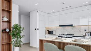 A modern kitchen with white cabinets, a marble countertop, and two bar stools.