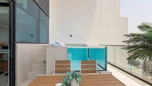 A modern balcony with a wooden table, chairs, and a potted plant.
