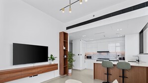 A modern living room with a flat-screen TV, wooden entertainment unit, and a seating area with ottomans.
