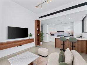 A modern living room with a flat-screen TV, wooden entertainment unit, and a seating area with ottomans.