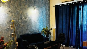 Un salon moderne avec un canapé bleu foncé, une table basse, une table à manger avec des chaises, un ventilateur de plafond et un appareil de climatisation.