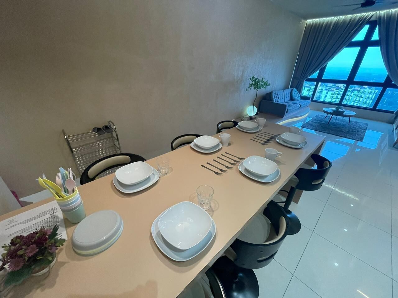A dining area with a table set for six, a plant, and a view of the city through large windows.