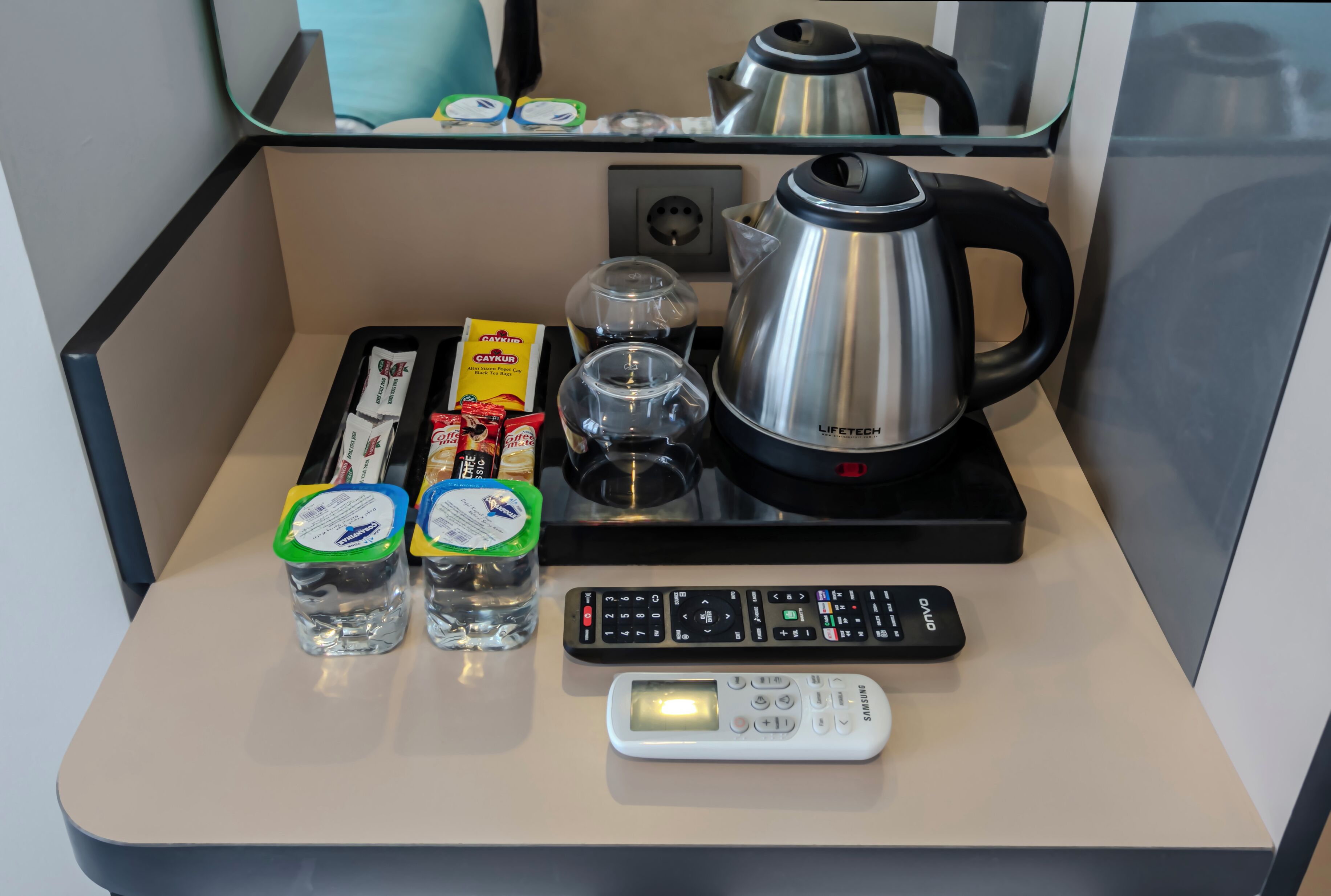 A kitchenette with a coffee maker, kettle, remote controls, and a digital scale.