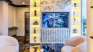 Un salón moderno con un televisor de pantalla plana grande, paredes de mármol y varios objetos decorativos en estanterías.