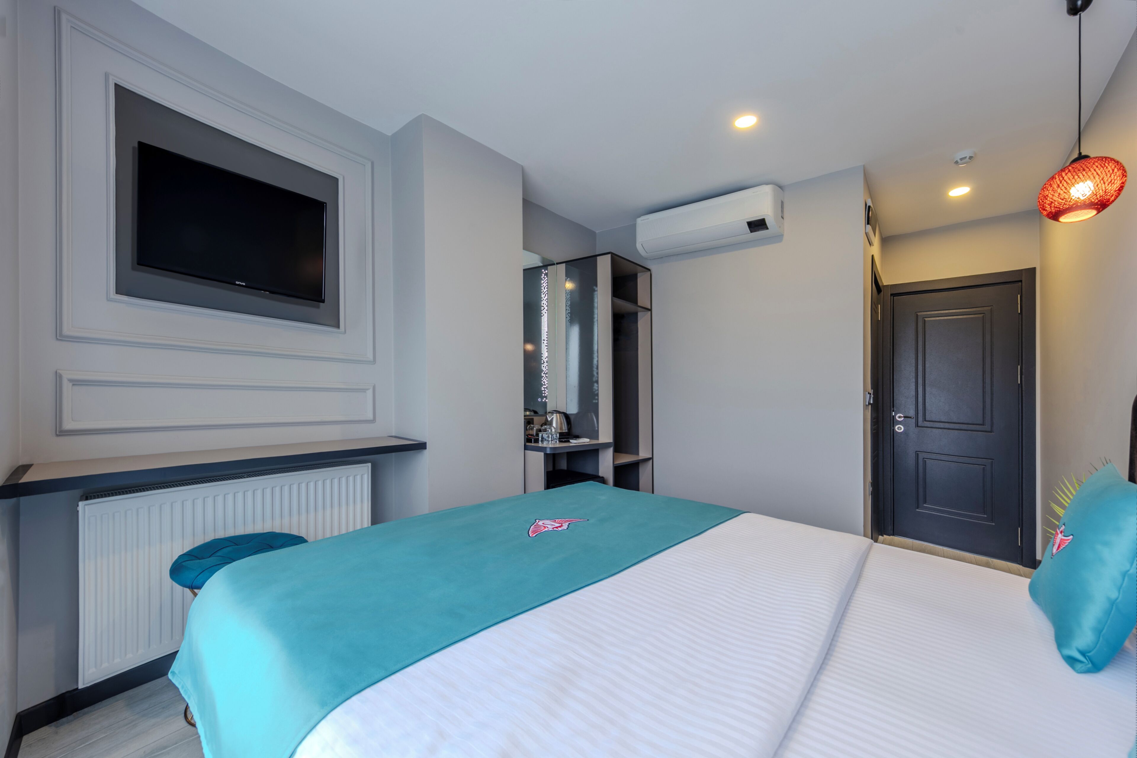 A modern hotel room with a large bed, a flat-screen TV mounted on the wall, a wardrobe, and a door.