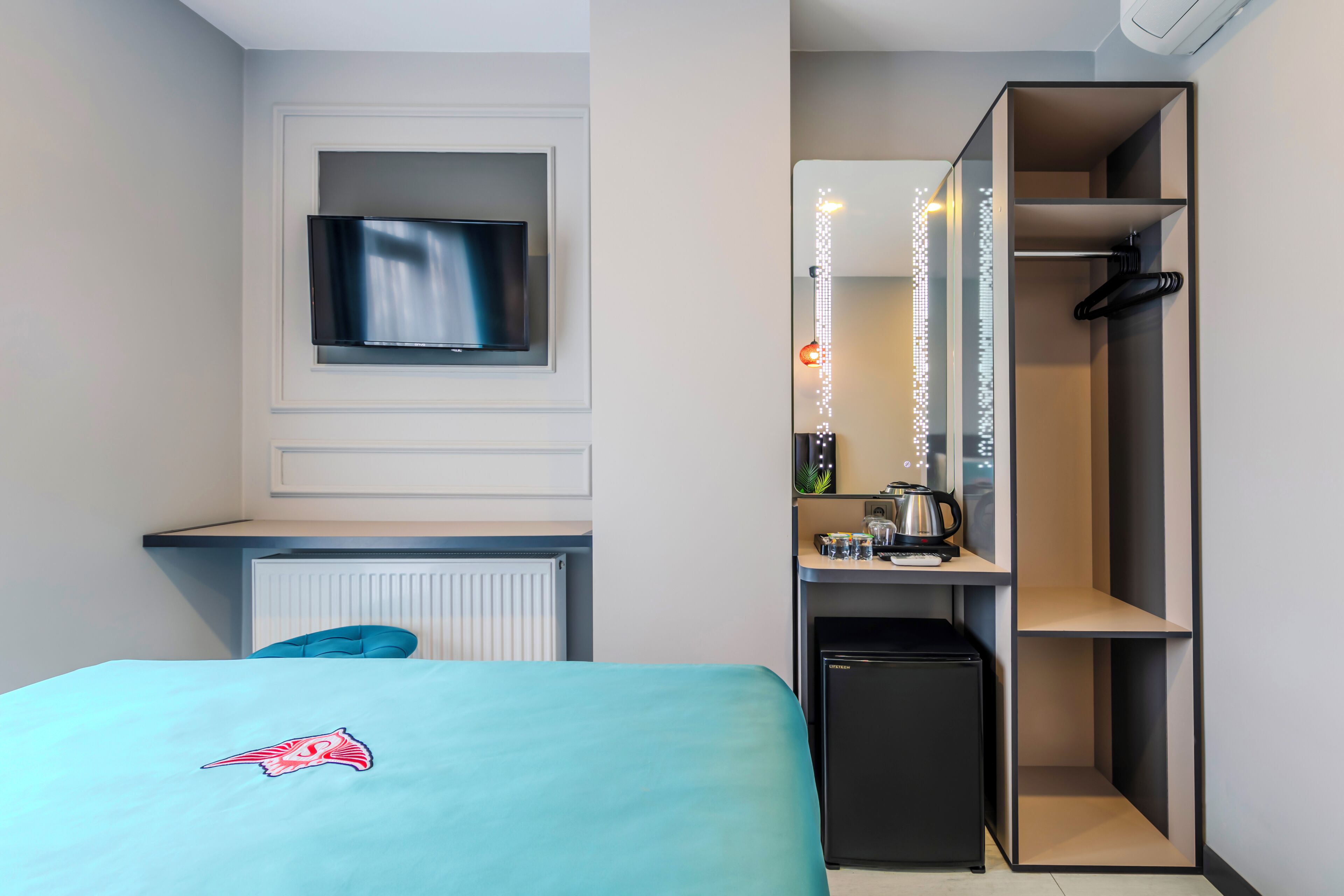 Een moderne hotelkamer met een bed, een klein bureau, een televisie, een spiegel en een minibar.