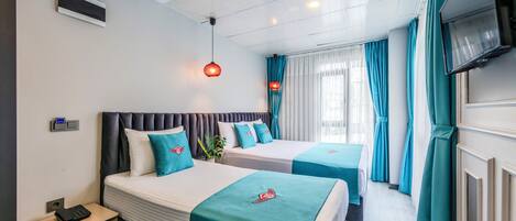 A hotel room with two beds, a TV, a phone, and a window with curtains.