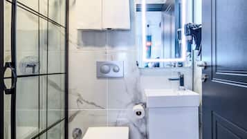 Un baño moderno con cabina de ducha de vidrio, inodoro, lavabo y espejo con iluminación integrada.