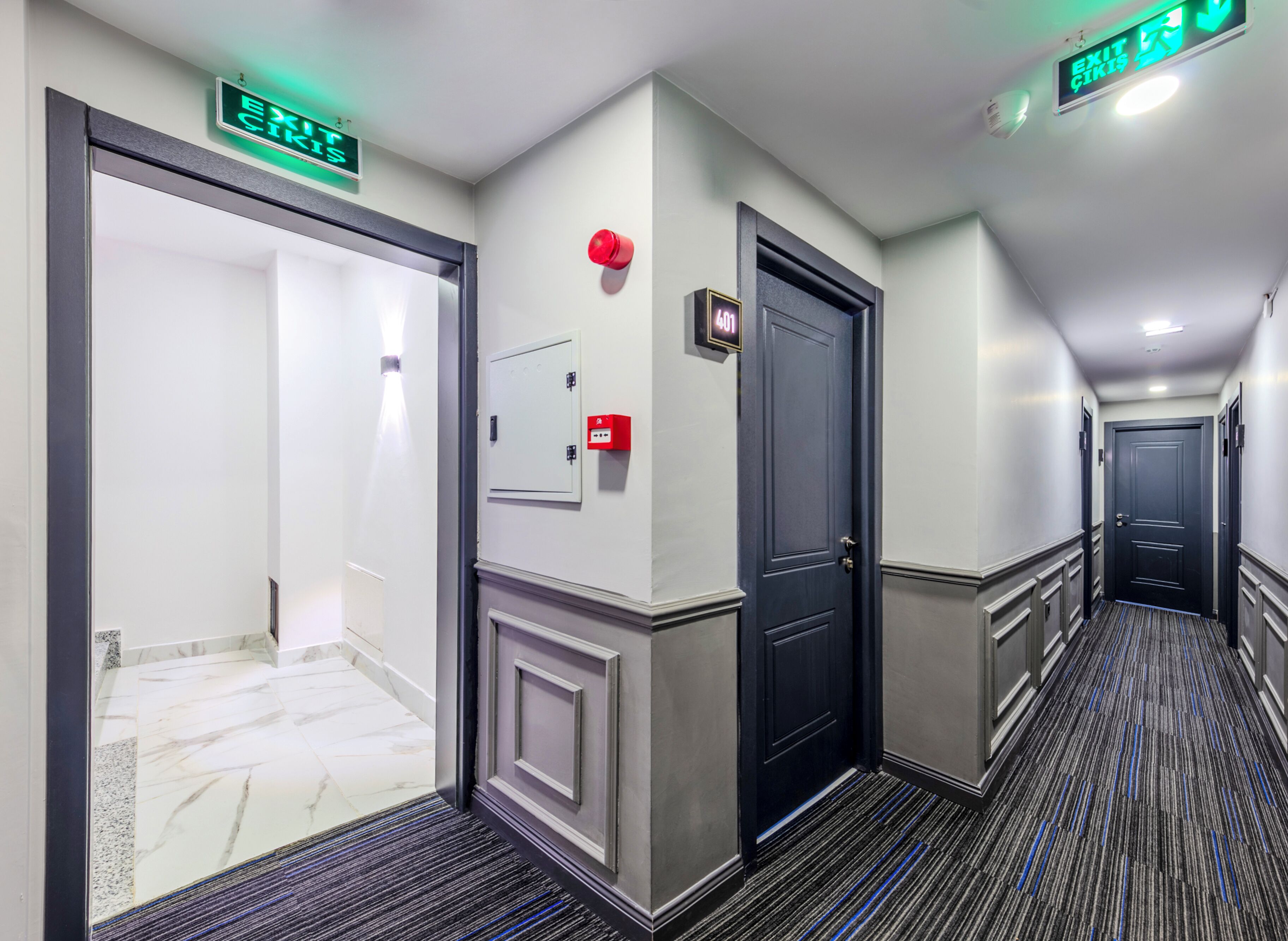 A hotel hallway with a marble floor, a black door, and an exit sign.
