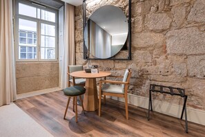 A room with a stone wall, a round table with two chairs, a mirror, and a window with curtains.