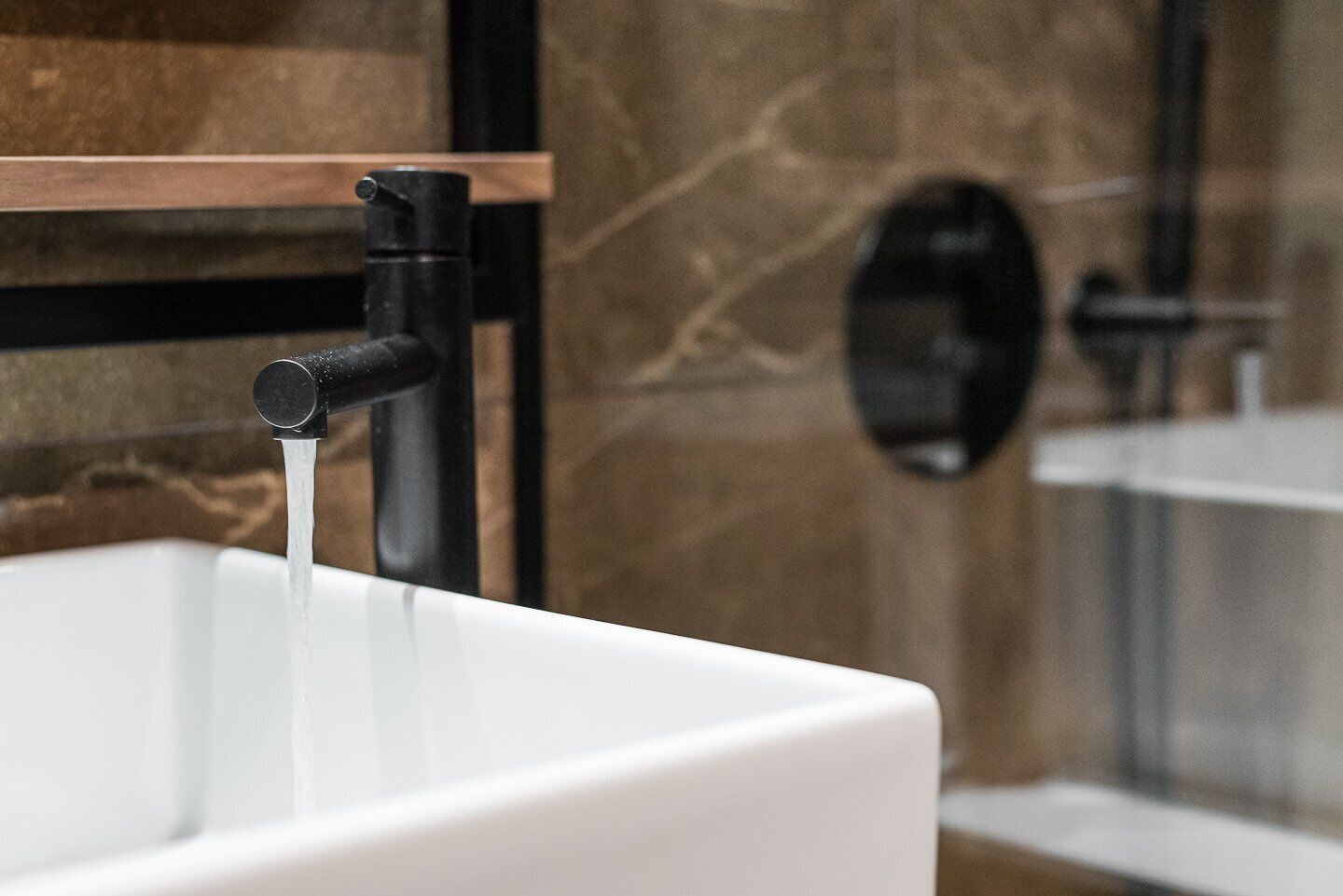 A bathroom with a white sink, a black faucet, and a marble wall.