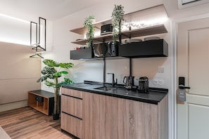 A modern kitchen with wooden cabinets, a black countertop, and a built-in microwave. There are two plants, a hanging light, and a door with a lock. - Guestready - Mercadores 150 (Porto)