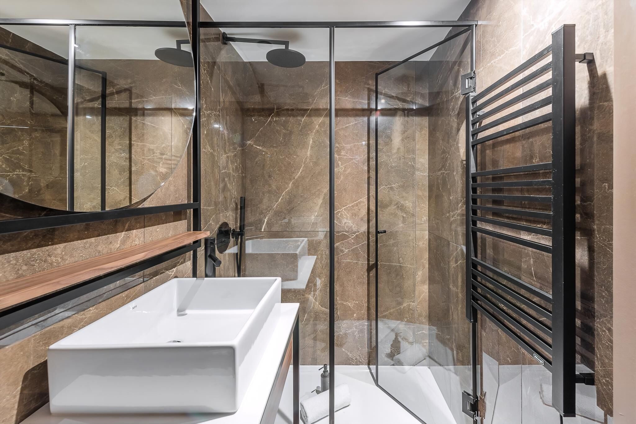 A modern bathroom with a glass-enclosed shower, a white sink, and a towel rack.