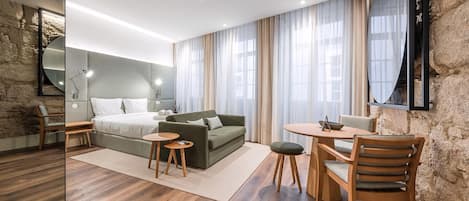 Ett modernt hotellrum med en vägg som har en dekorativ stenbeklädnad, en stor säng, en grön soffa, en matplats med bord och stolar samt en stor spegel.