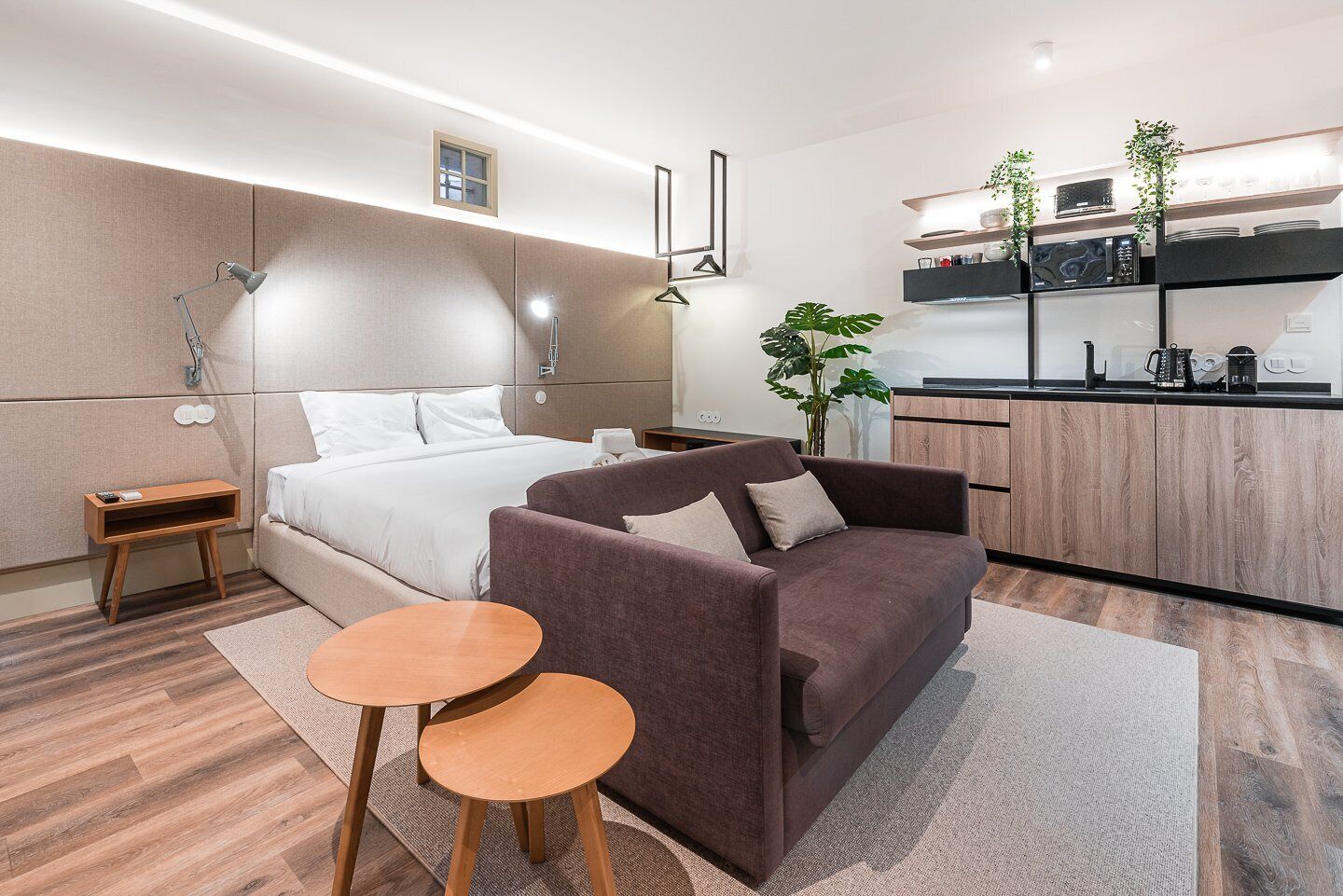 A modern hotel room with a bed, a sofa, a small table, and a kitchenette.