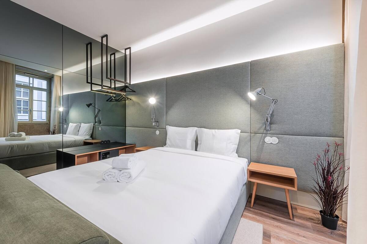 A modern hotel room with a large bed, bedside tables, a mirror, and a potted plant.