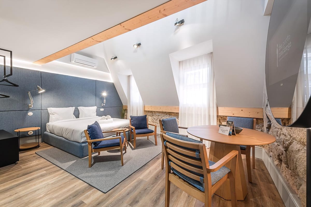 A modern bedroom with a bed, seating area, and a dining table.
