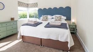 Quarto com cama, mesa de cabeceira, cômoda e janela com vista para o verde.