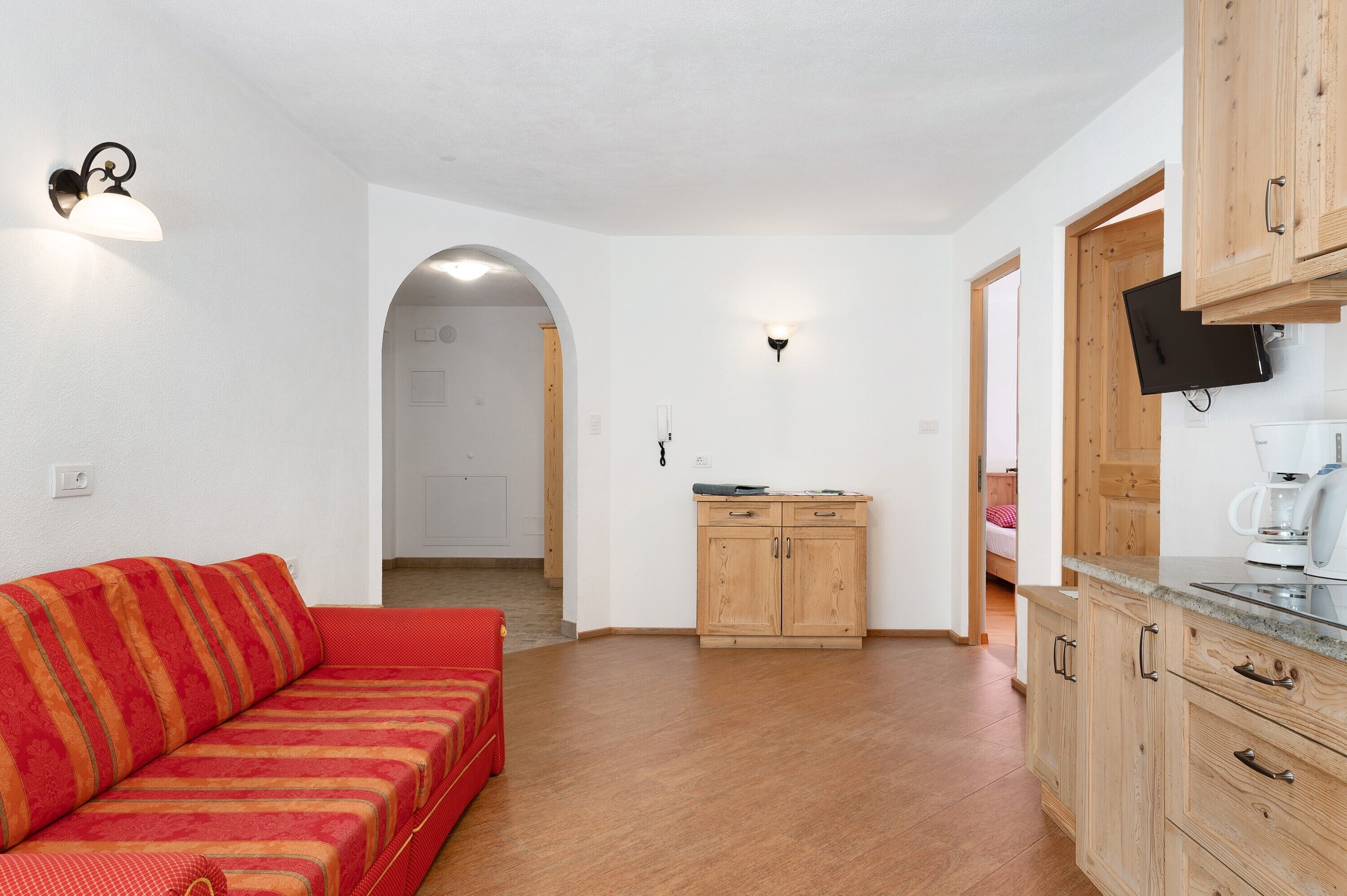 Ein gemütlicher Wohnbereich mit einer Couch, Holzschränken, einem Fernseher und einer Küchenzeile.