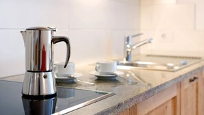 Uma cozinha com cafeteira de aço inoxidável, chávenas brancas, uma pia e bancada de granito.