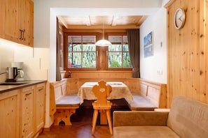 Interior de una cabaña de madera con una mesa de comedor, bancos, un sofá y una ventana con vistas a árboles.