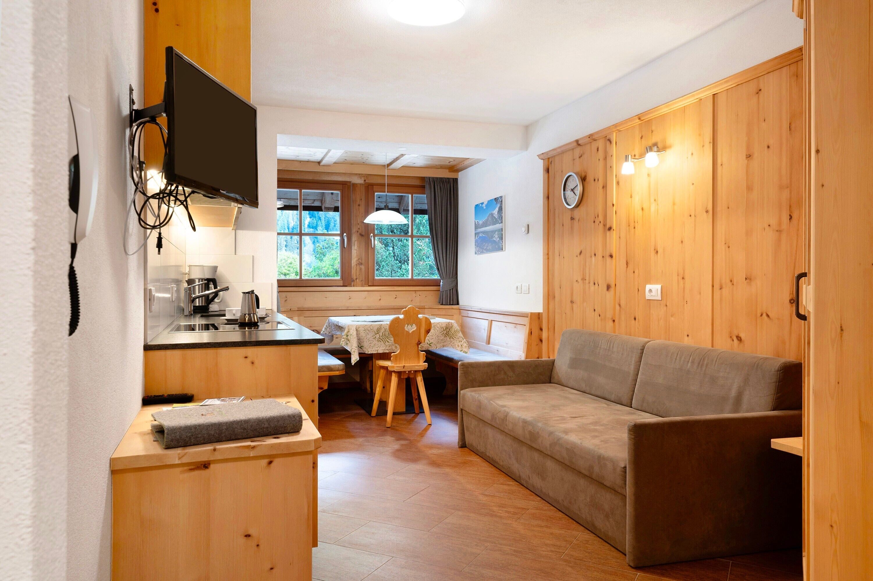 Ett litet rum med en väggpanel av trä, en soffa, ett litet bord, en tv som är monterad på väggen och ett fönster med utsikt över grönområden.