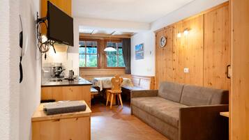 Ett litet rum med en väggpanel av trä, en soffa, ett litet bord, en tv som är monterad på väggen och ett fönster med utsikt över grönområden.